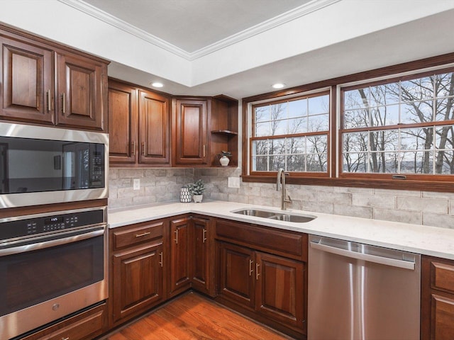 kitchen featuring sink, light stone counters, crown molding, appliances with stainless steel finishes, and light wood-type flooring