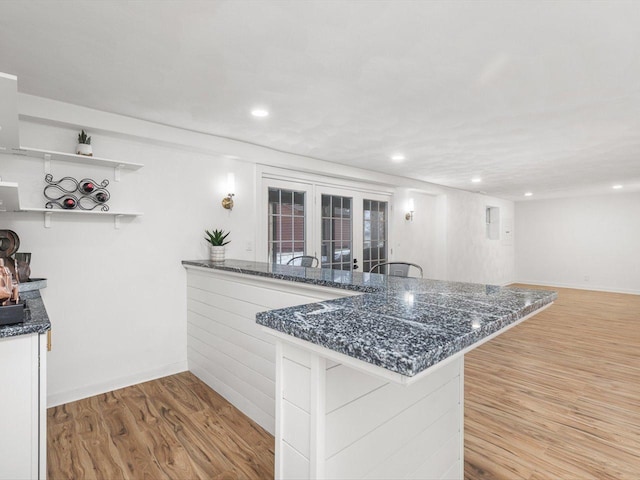 kitchen featuring kitchen peninsula, light wood-type flooring, white cabinetry, and dark stone counters