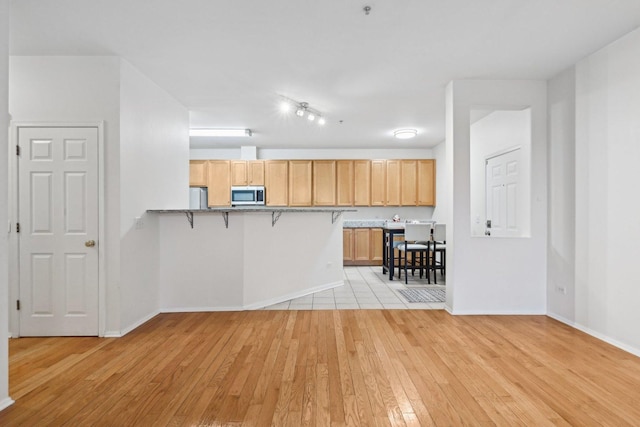 kitchen with kitchen peninsula, light brown cabinetry, white refrigerator, light hardwood / wood-style flooring, and a breakfast bar area