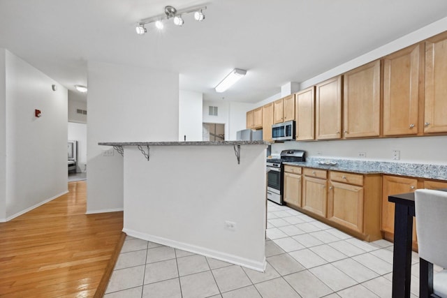 kitchen featuring a kitchen breakfast bar, light tile patterned flooring, light stone counters, and stainless steel appliances