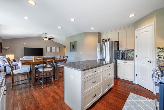 kitchen with vaulted ceiling, appliances with stainless steel finishes, tasteful backsplash, a center island, and dark stone countertops