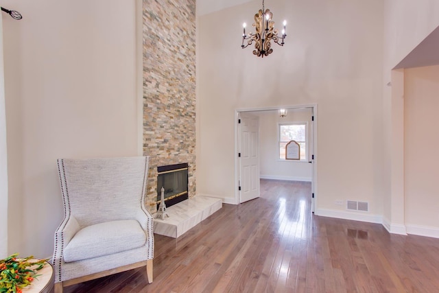 sitting room featuring a towering ceiling, hardwood / wood-style flooring, a notable chandelier, and a stone fireplace