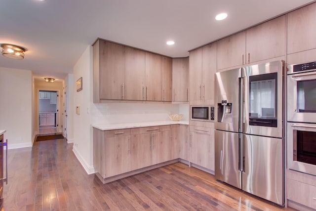 kitchen with tasteful backsplash, appliances with stainless steel finishes, wood-type flooring, and light brown cabinets