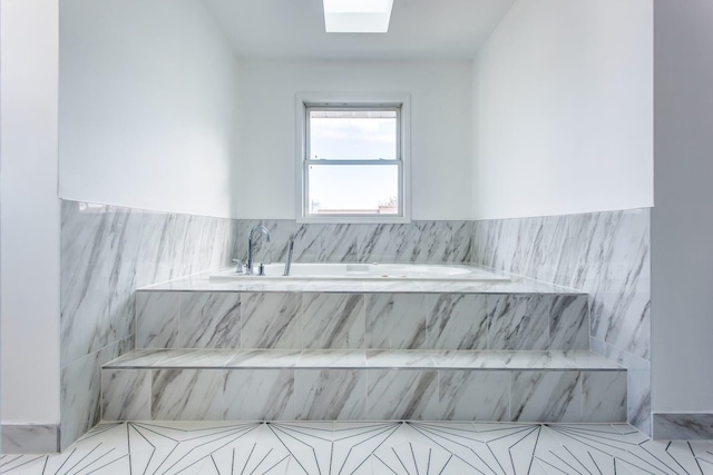 bathroom with a skylight and tiled bath