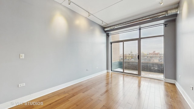 spare room featuring light hardwood / wood-style floors, a wall of windows, and track lighting