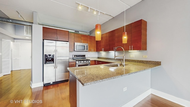 kitchen featuring pendant lighting, kitchen peninsula, sink, light stone countertops, and stainless steel appliances