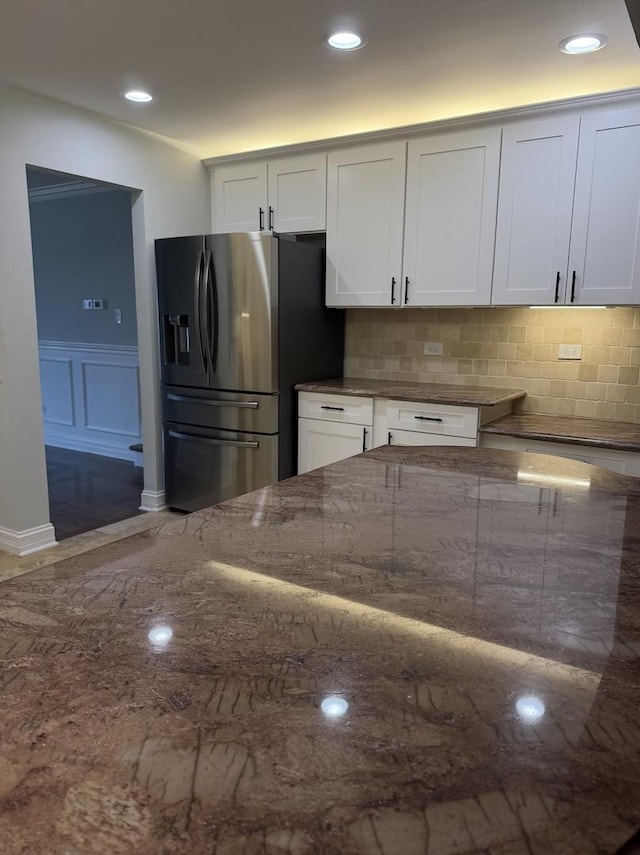 kitchen with white cabinets, tasteful backsplash, stainless steel fridge, and dark stone counters