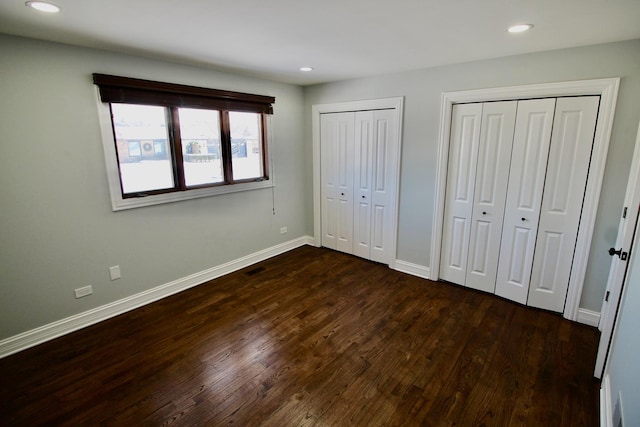 unfurnished bedroom with dark hardwood / wood-style flooring and multiple closets