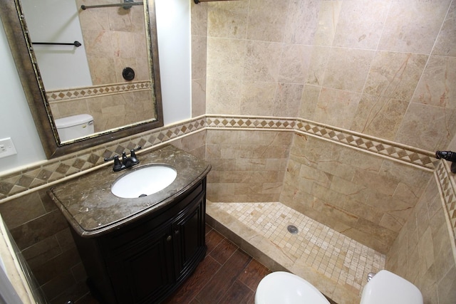 bathroom featuring vanity, tiled shower, tile walls, and toilet