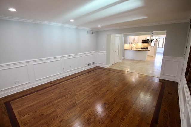 empty room featuring sink, ornamental molding, light hardwood / wood-style floors, and a chandelier