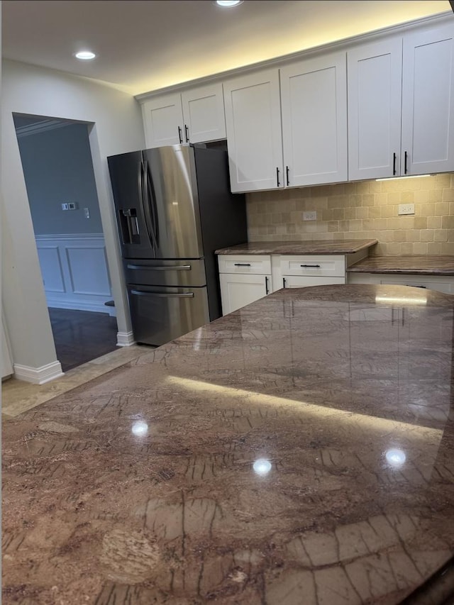 kitchen with stainless steel refrigerator with ice dispenser, backsplash, stone counters, and white cabinets