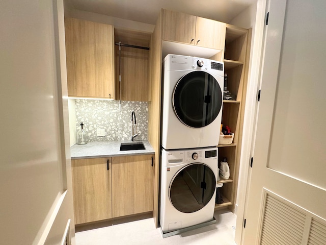 washroom featuring stacked washer and dryer, sink, and cabinets