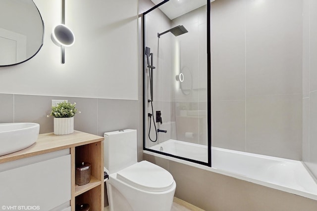 full bathroom with tile walls, bath / shower combo with glass door, vanity, and toilet