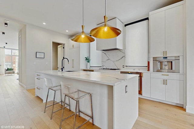 kitchen with sink, stainless steel oven, white cabinetry, and an island with sink