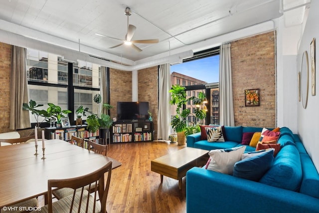 living room featuring ceiling fan, wood-type flooring, and brick wall