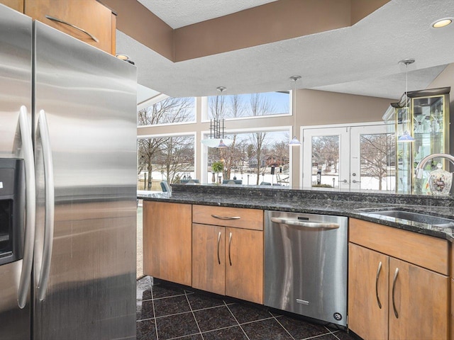 kitchen featuring appliances with stainless steel finishes, dark stone counters, a textured ceiling, decorative light fixtures, and sink