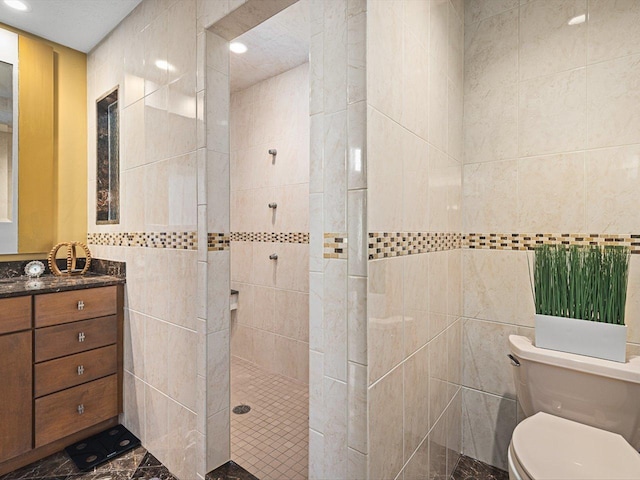 bathroom with vanity, toilet, tiled shower, and tile walls