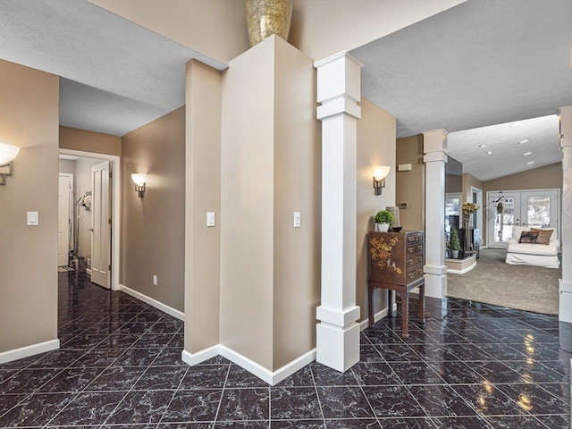 corridor featuring ornate columns, french doors, a textured ceiling, and vaulted ceiling