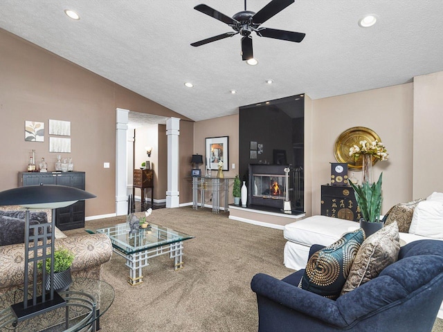 carpeted living room with a large fireplace, a textured ceiling, ornate columns, lofted ceiling, and ceiling fan