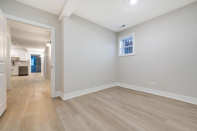 unfurnished room featuring sink, light hardwood / wood-style floors, and beam ceiling