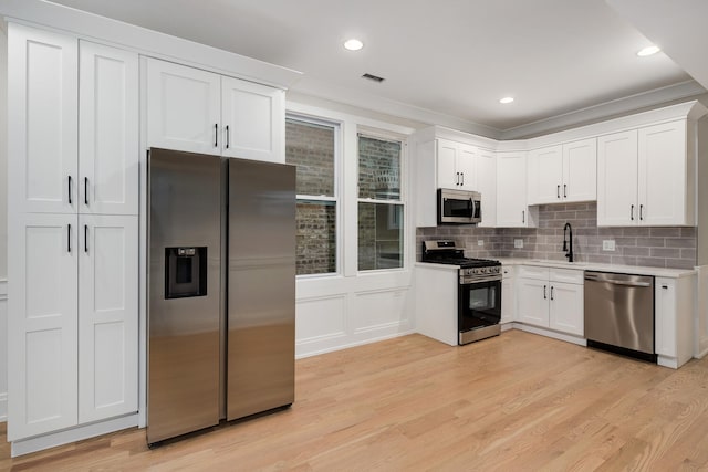 kitchen with sink, white cabinetry, light hardwood / wood-style flooring, decorative backsplash, and appliances with stainless steel finishes