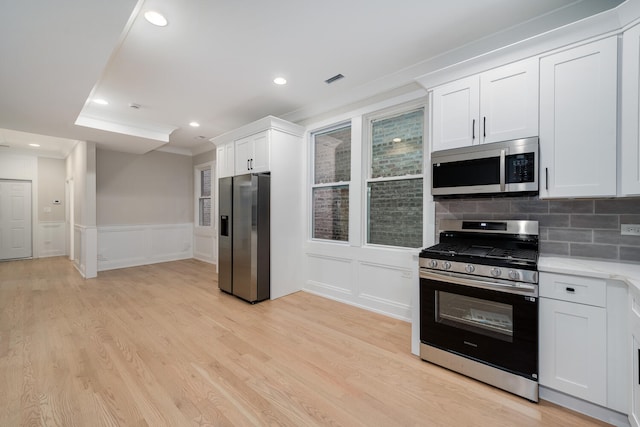 kitchen featuring white cabinets, light wood-type flooring, appliances with stainless steel finishes, and crown molding