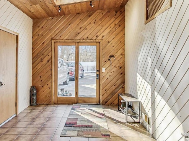 doorway to outside featuring a towering ceiling, wooden ceiling, a skylight, wooden walls, and tile patterned floors