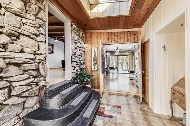 hall with a skylight, wood walls, wooden ceiling, and light tile patterned flooring