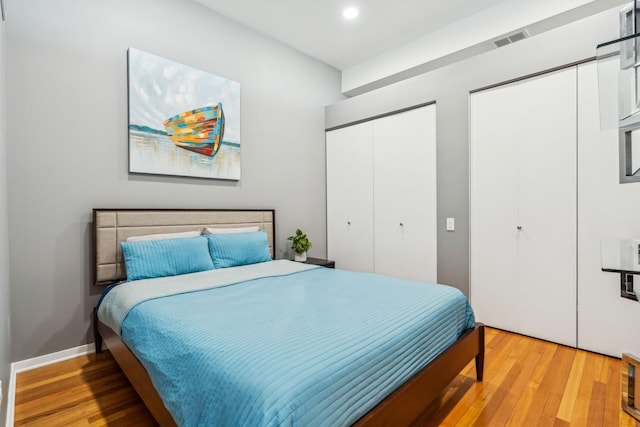 bedroom with light hardwood / wood-style floors and two closets