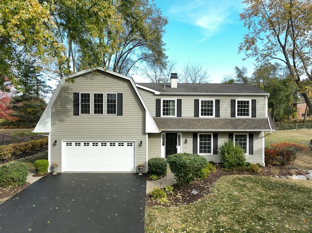 colonial inspired home with driveway, a garage, a gambrel roof, roof with shingles, and fence