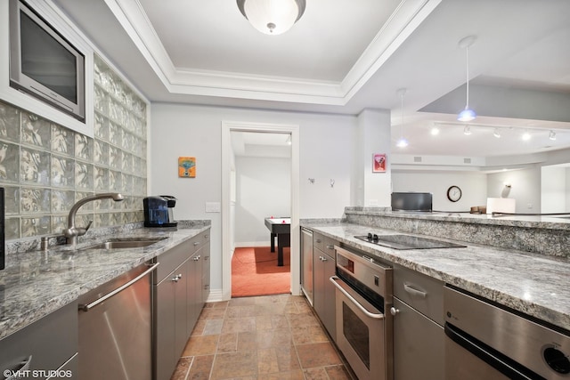 kitchen featuring stainless steel appliances, sink, decorative light fixtures, light stone counters, and a tray ceiling