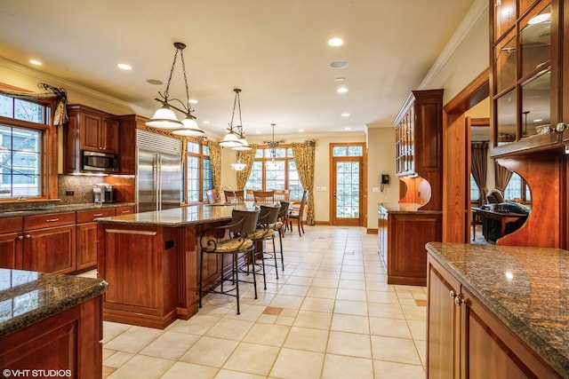 kitchen with decorative light fixtures, stainless steel appliances, a breakfast bar, light tile patterned floors, and a kitchen island with sink