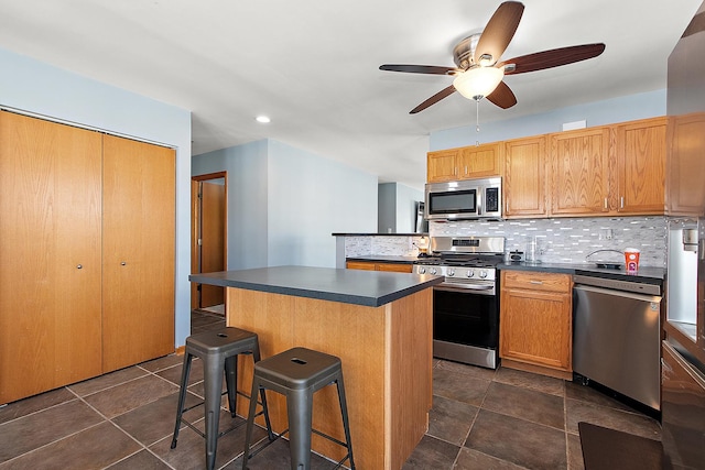 kitchen featuring appliances with stainless steel finishes, a center island, ceiling fan, a kitchen bar, and backsplash