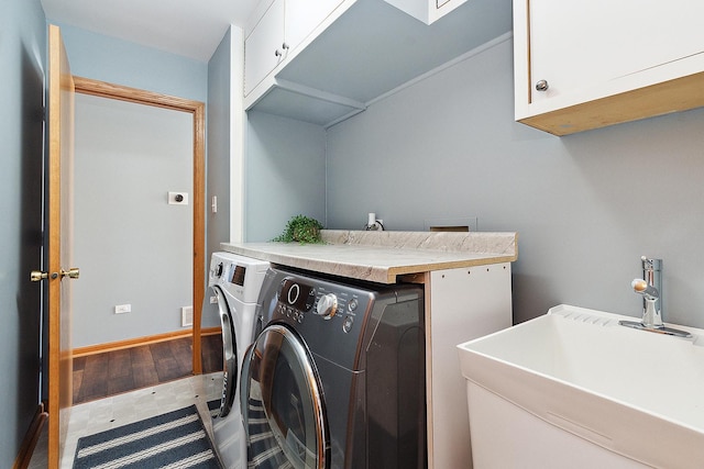 clothes washing area featuring sink, washing machine and dryer, hardwood / wood-style flooring, and cabinets