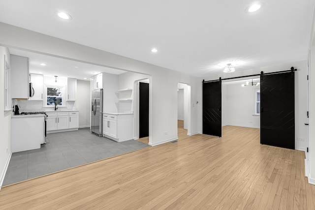 unfurnished living room with a barn door, light wood-type flooring, and sink