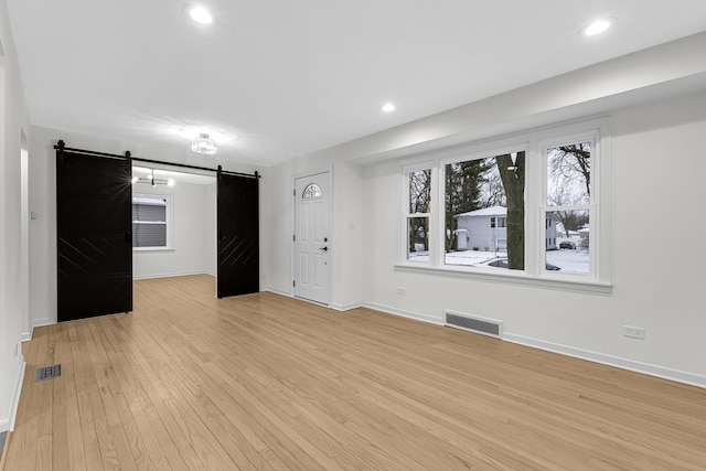 unfurnished living room featuring a barn door and light hardwood / wood-style floors