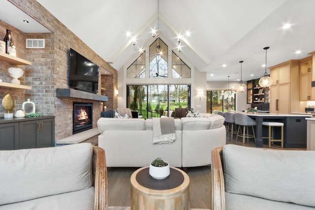 living room with visible vents, high vaulted ceiling, a notable chandelier, wood finished floors, and a lit fireplace