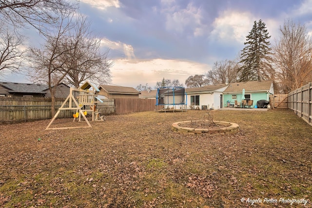 yard at dusk featuring a playground, a trampoline, and a patio