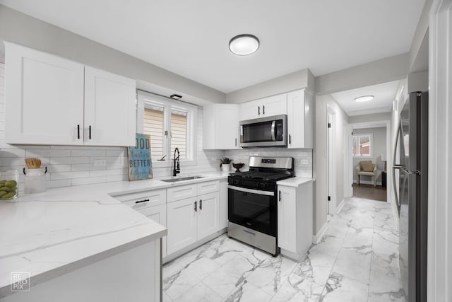 kitchen featuring appliances with stainless steel finishes, light stone countertops, sink, white cabinetry, and tasteful backsplash