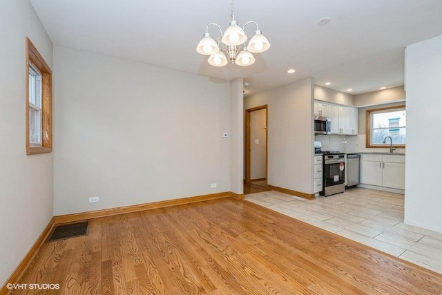 unfurnished living room featuring sink, light wood-type flooring, and a chandelier