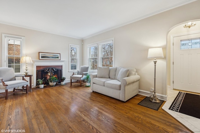 living room with hardwood / wood-style flooring, ornamental molding, an inviting chandelier, and a brick fireplace