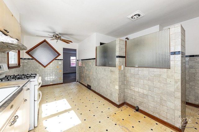 kitchen featuring ceiling fan, white range with gas stovetop, and tile walls