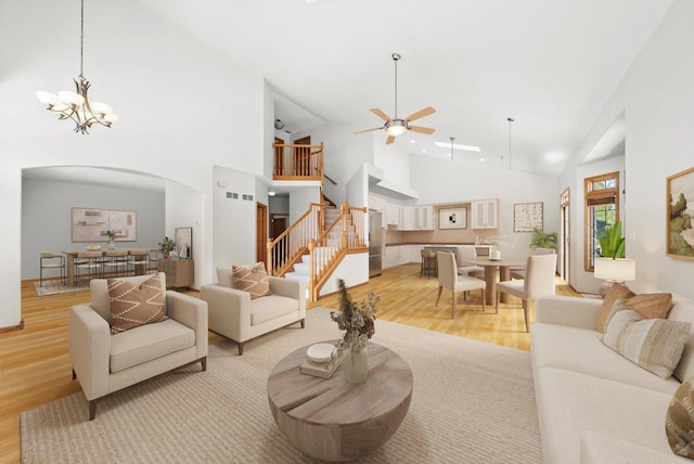 living room with high vaulted ceiling, ceiling fan with notable chandelier, and light hardwood / wood-style floors