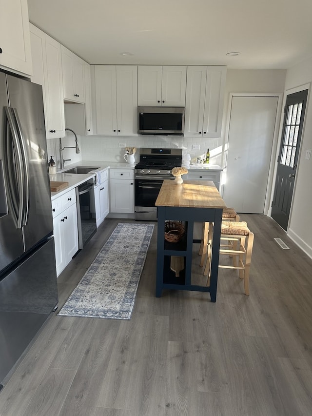 kitchen with white cabinetry, hardwood / wood-style flooring, wooden counters, stainless steel appliances, and tasteful backsplash