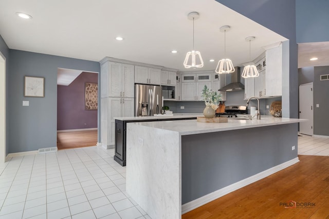 kitchen featuring pendant lighting, kitchen peninsula, sink, appliances with stainless steel finishes, and wall chimney exhaust hood