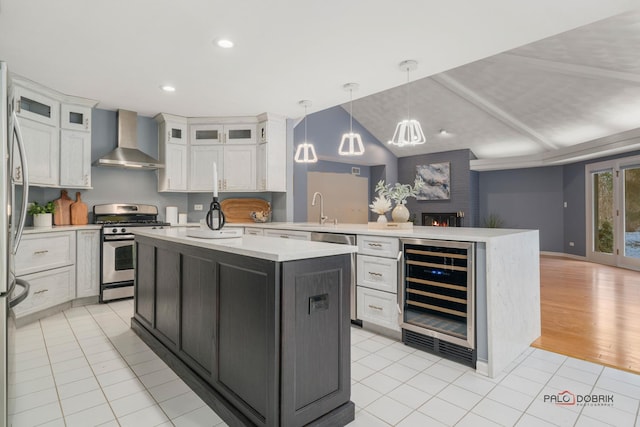 kitchen with white cabinetry, wine cooler, stainless steel gas stove, wall chimney range hood, and pendant lighting