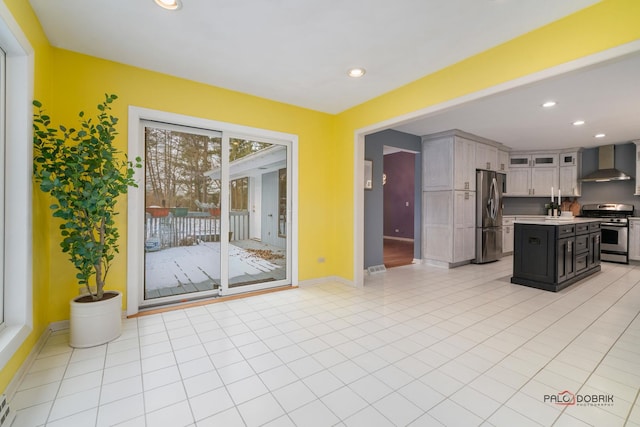 kitchen featuring light tile patterned floors, wall chimney range hood, stainless steel appliances, and a center island