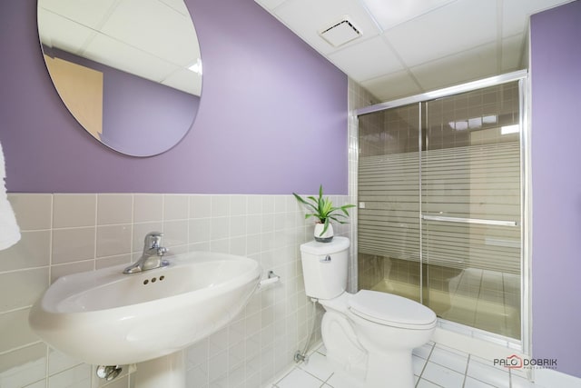 bathroom featuring tile patterned floors, a shower with door, sink, tile walls, and toilet