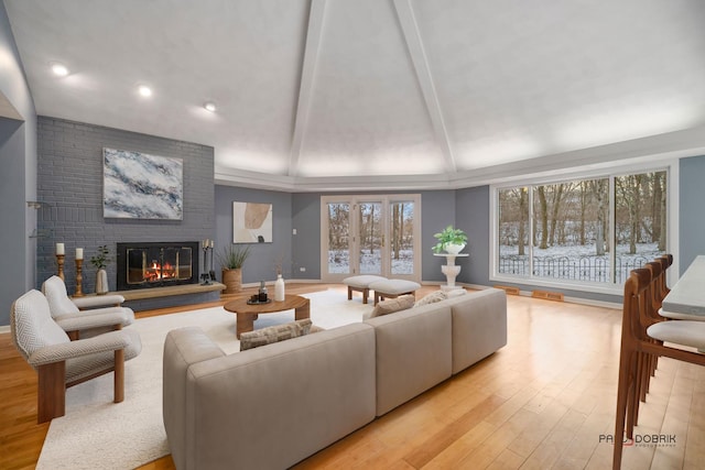 living room with a brick fireplace, light hardwood / wood-style flooring, lofted ceiling with beams, and a healthy amount of sunlight