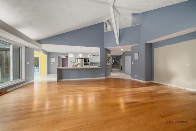 unfurnished living room featuring light hardwood / wood-style floors, high vaulted ceiling, and beamed ceiling